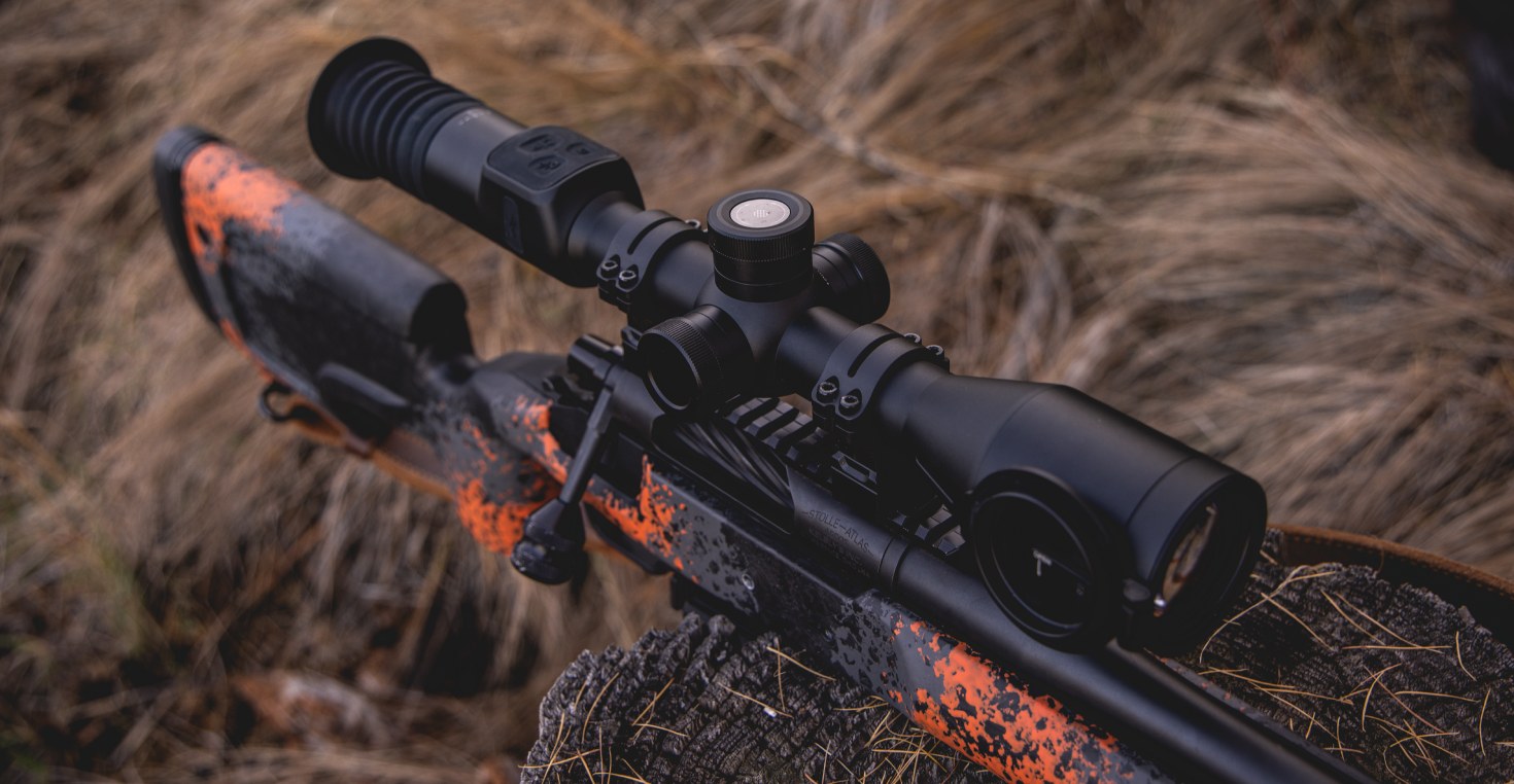 Field Testing the PARD Nightstalker EX Weapon-Mounted Scope Close-up view of the PARD Nightstalker EX mounted on a rugged, orange-camo hunting rifle, photographed outdoors in tall grass. The image highlights the scope’s compact design, precision controls, and field-ready durability.