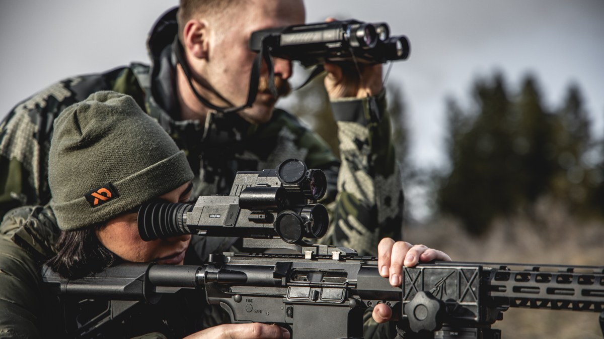 Hunter scanning terrain with night vision binoculars during daylight, showcasing detection range and multispectral awareness.